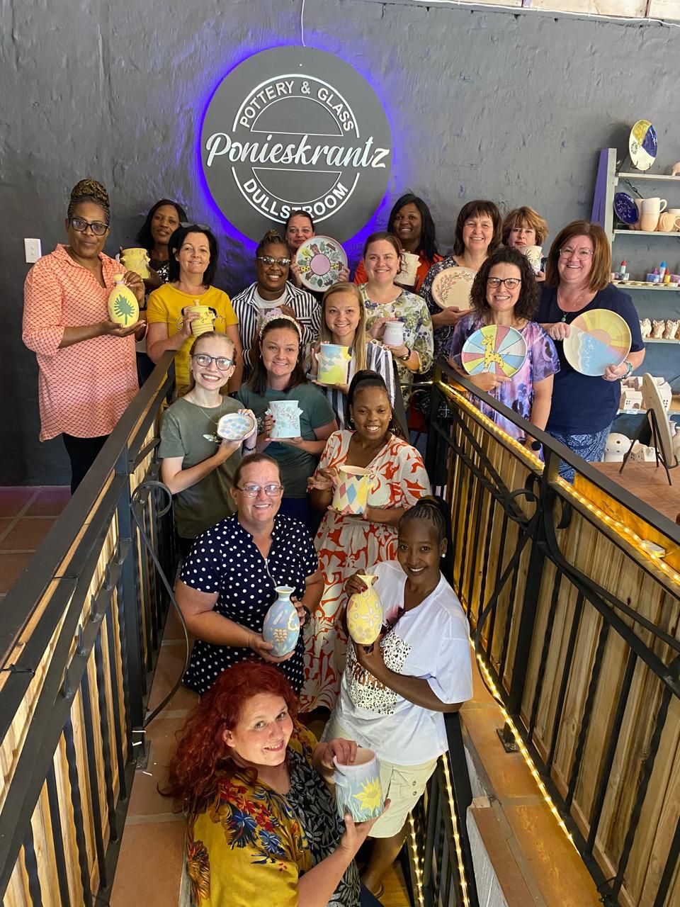 A large group of teachers proudly holding the vases, mugs and plates they painted at Ponieskrantz