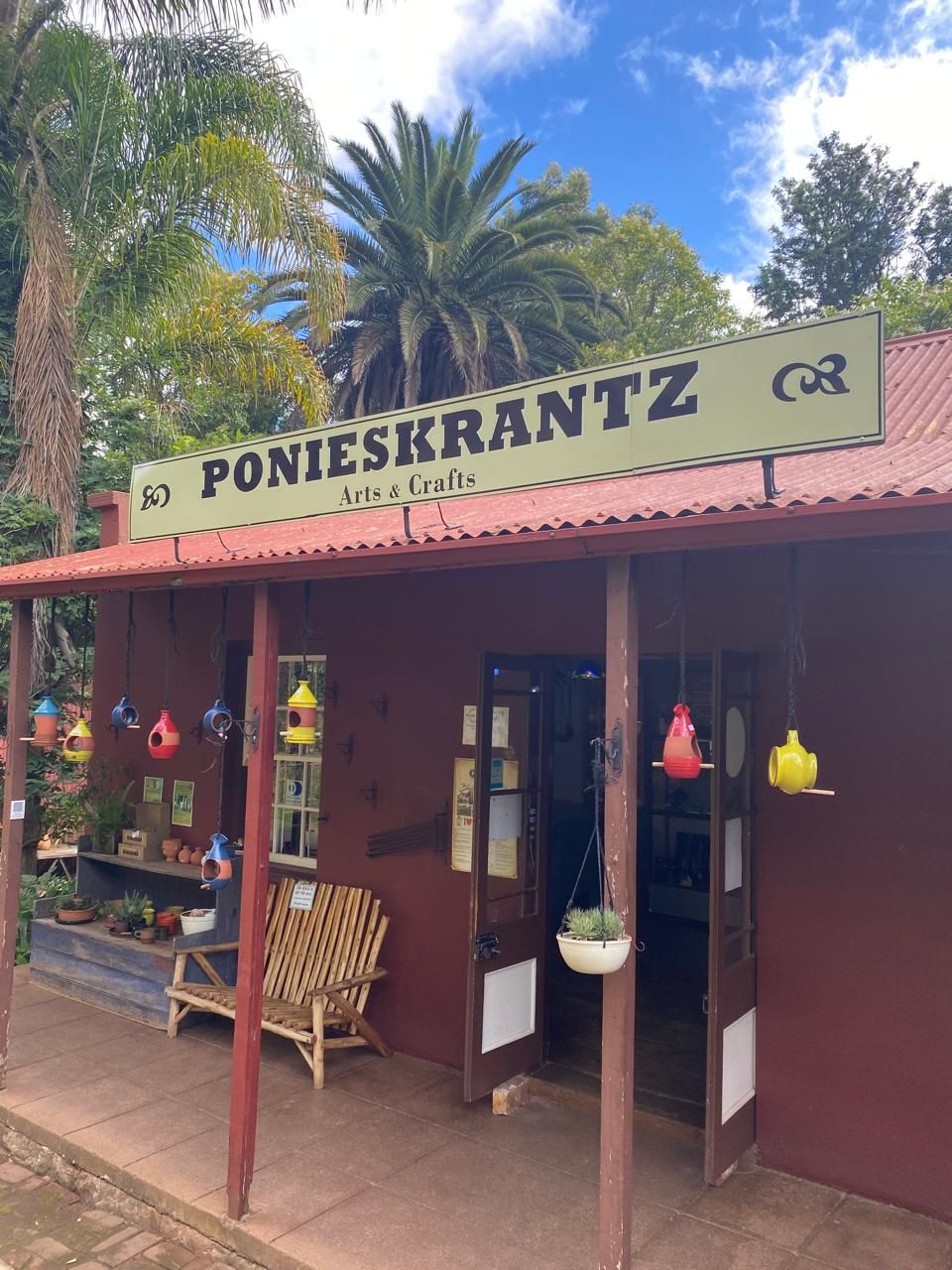 The front of the Ponieskrantz Arts & Crafts shop in Pilgrim's Rest, with colourful ceramic bird feeders hanging from the veranda
